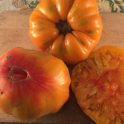 Trois tomates allemandes à rayures orange Tourne-Sol sur une planche à découper en bois.